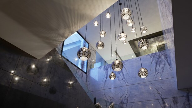 A modern interior with marble walls, hanging spherical light fixtures, and a geometric ceiling design.