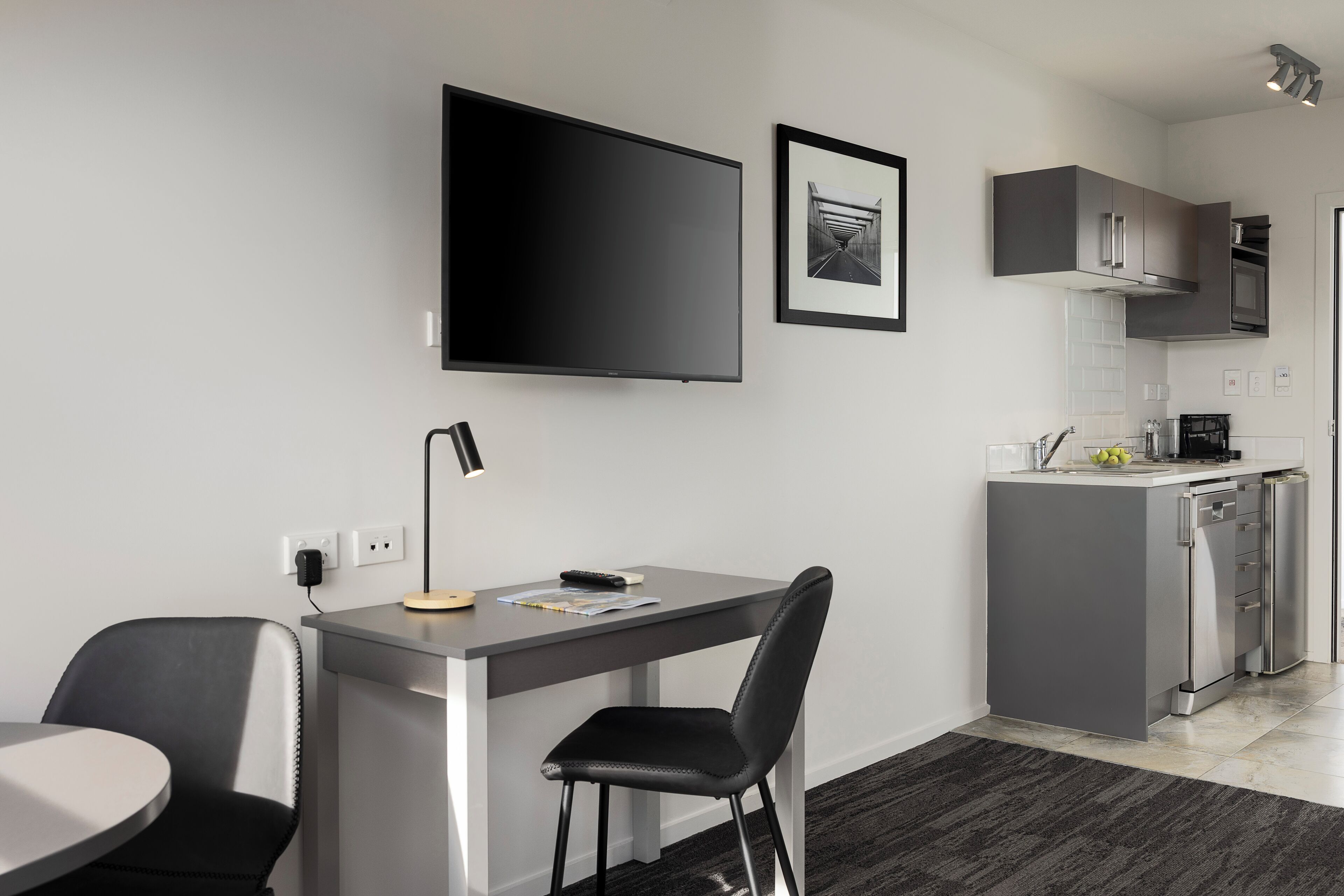 A modern kitchen with a flat-screen TV, a framed picture, and a dining area with a table and chairs.