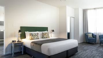 A hotel room with a large bed, a nightstand, a lamp, a chair, and a window with curtains.