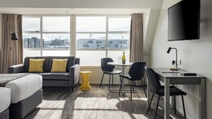 A modern hotel room with a large window, a sofa, a desk, and a bed.