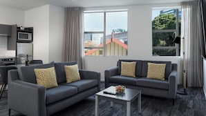 A modern living room with two grey sofas, a coffee table, and a view of buildings through large windows.