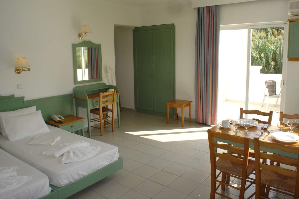 Ein Hotelzimmer mit zwei Betten, einem Schreibtisch, einem Stuhl, einem kleinen Tisch, einem Telefon und einem Fenster mit Vorhängen.