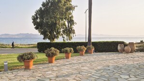 Un camino pavimentado con plantas en macetas, una carretera y vistas al mar con montañas al fondo.