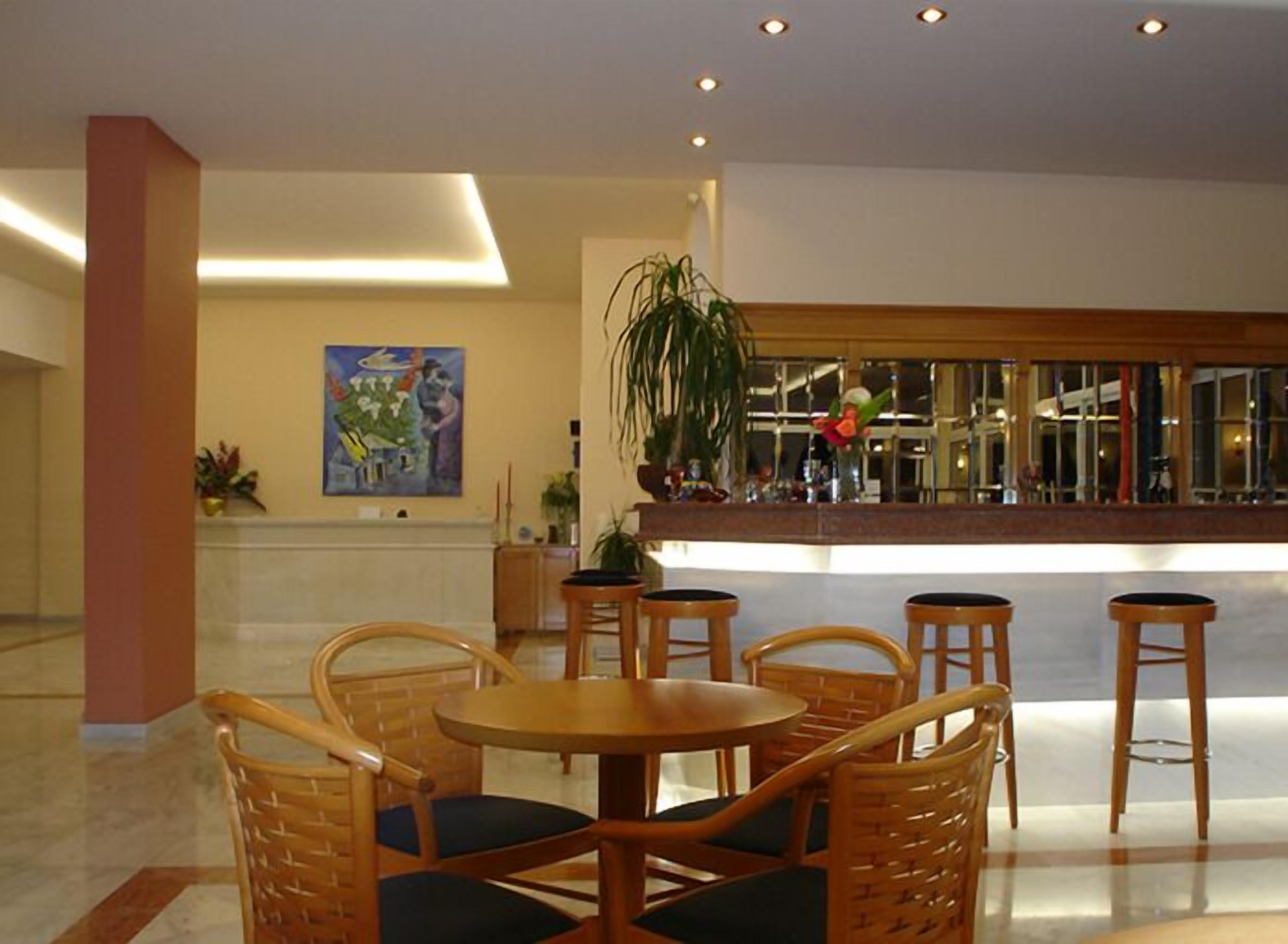 A lobby with a reception desk, a large potted plant, wicker chairs, and a painting on the wall.