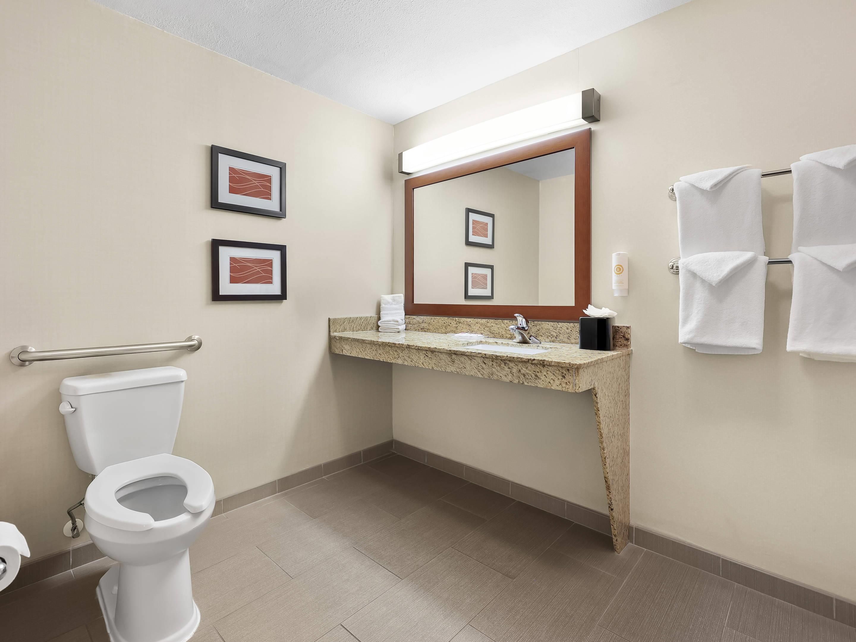 A hotel bathroom with a toilet, sink, mirror, framed pictures, and towels.