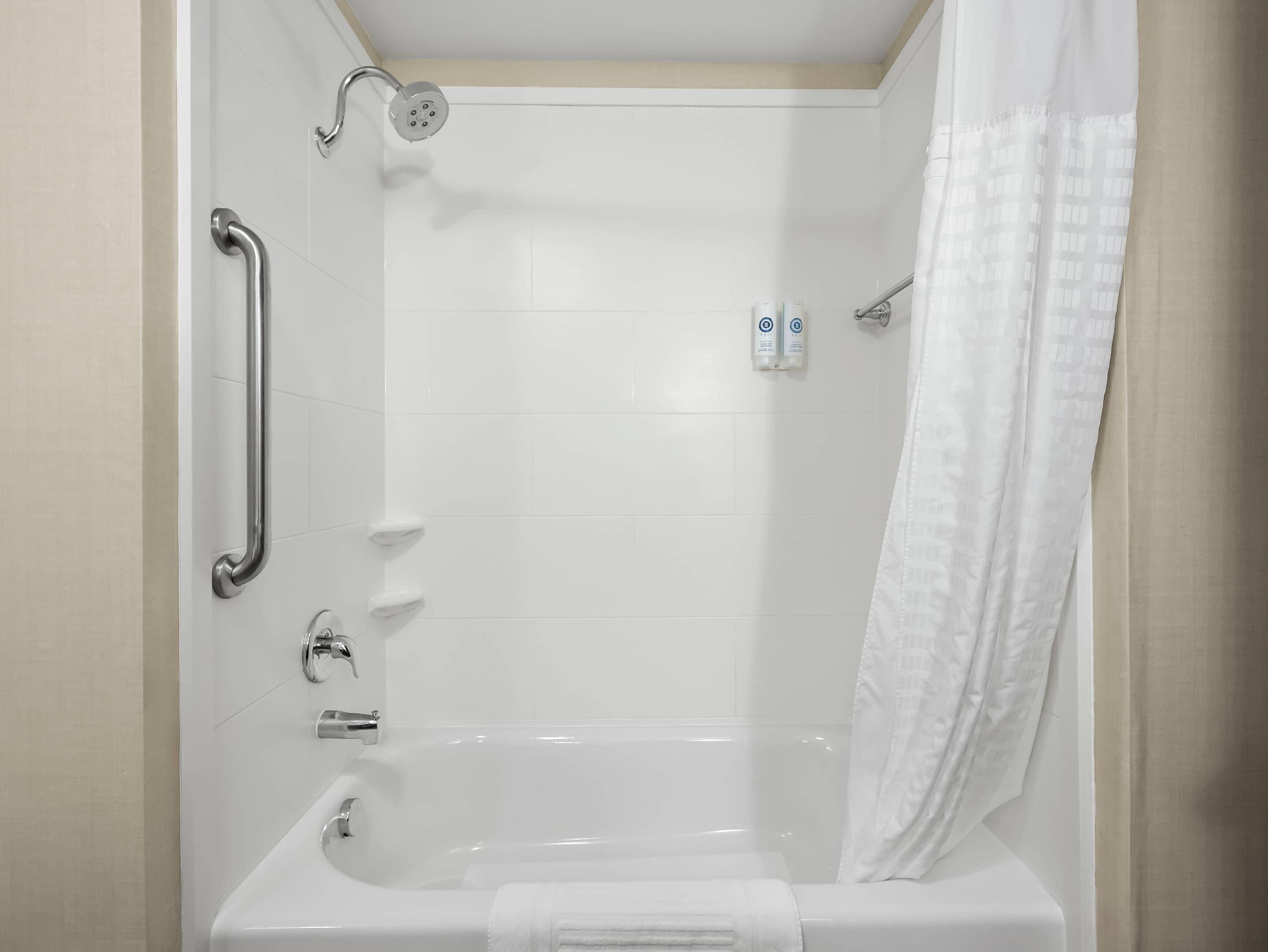 Ein schlichtes, weißes Badezimmer mit Badewanne, Duschkopf, Handlauf und Handtuchhalter.