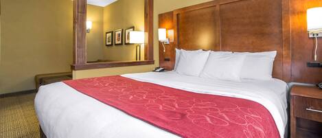A hotel room with a large bed, a wooden headboard, a nightstand, and a wall-mounted lamp.