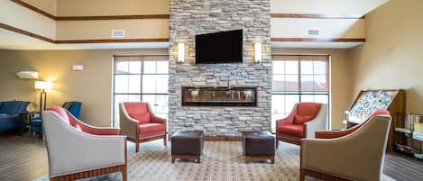 A spacious lobby with a stone fireplace, comfortable seating, and a large TV screen.
