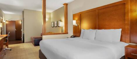 A hotel room with a large bed, a desk, a chair, a wardrobe, and a mirror.