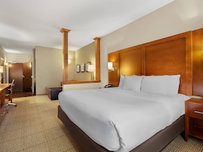 Una habitación de hotel con una cama grande, un escritorio, una silla, un armario y un espejo.