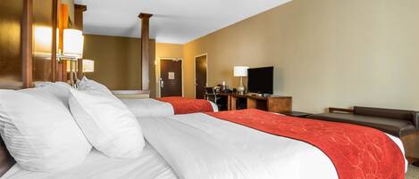 A hotel room with two beds, a desk, a television, and a lamp.