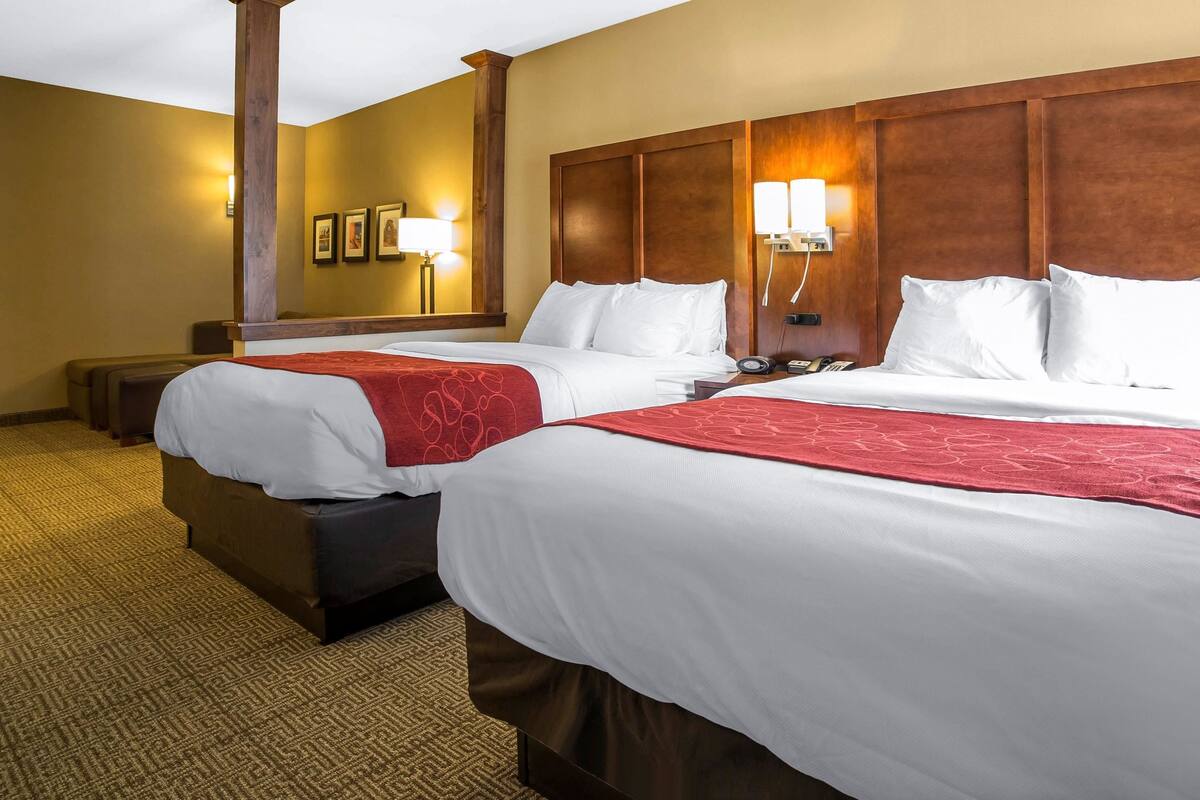 Habitación de hotel con dos camas, cada una con ropa blanca y detalles rojos, cabeceros de madera y piso alfombrado.