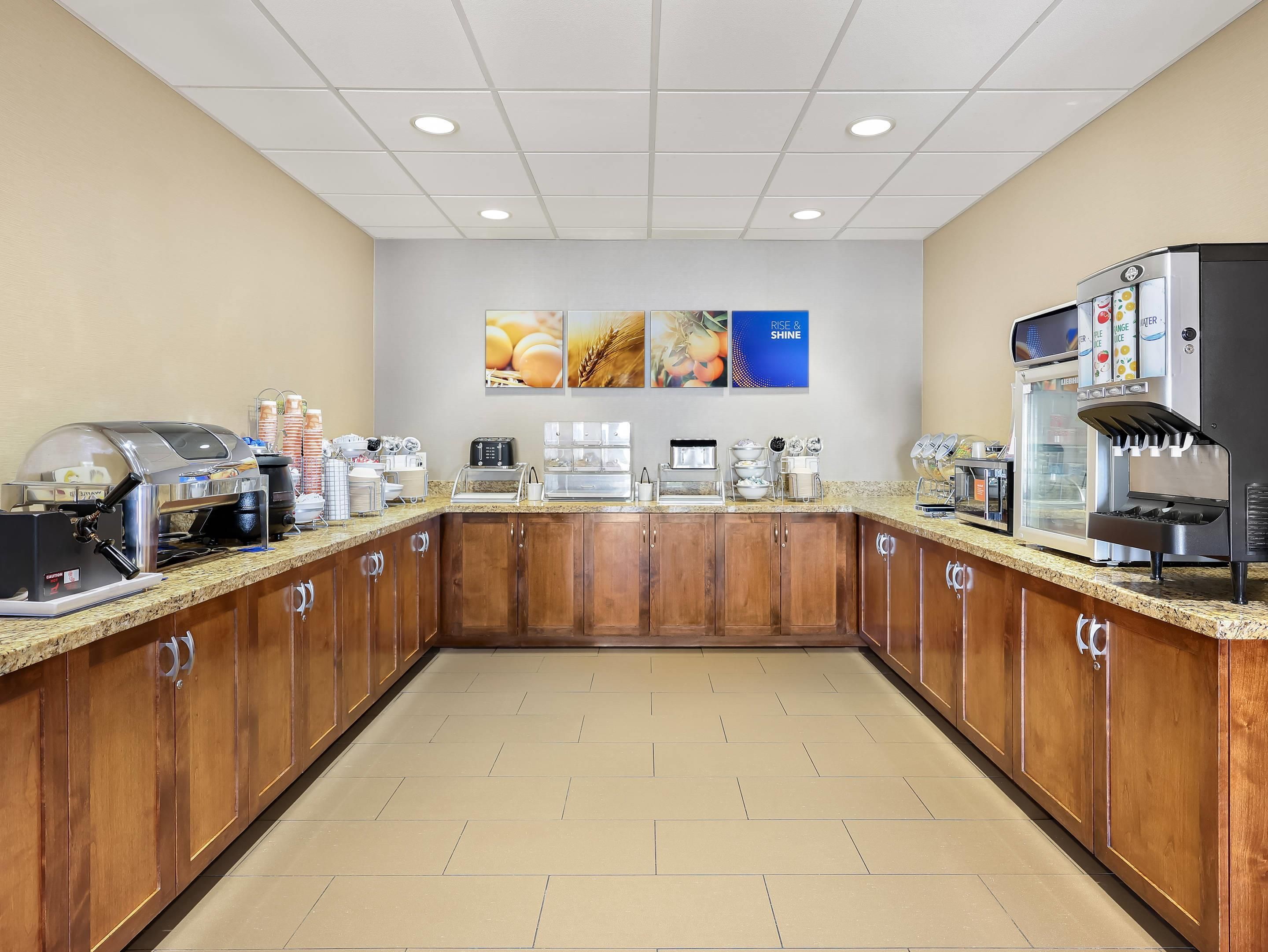 Un área de desayuno con una máquina de café, una exhibición de pan y un dispensador de jugo.