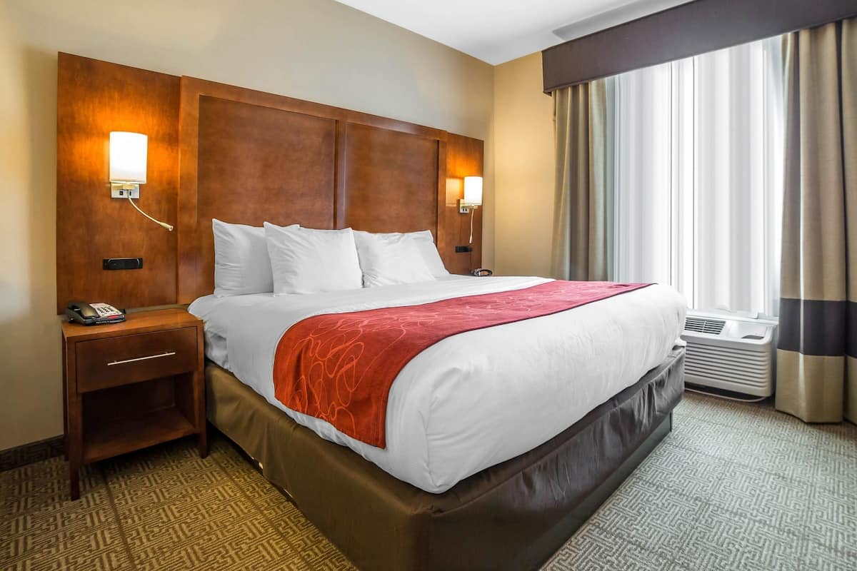 Habitación de hotel con una cama grande, dos mesitas de noche, un teléfono y una ventana con cortinas.