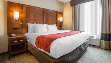 Ein Hotelzimmer mit einem großen Bett, zwei Nachttischen, einem Telefon und einem Fenster mit Vorhängen.