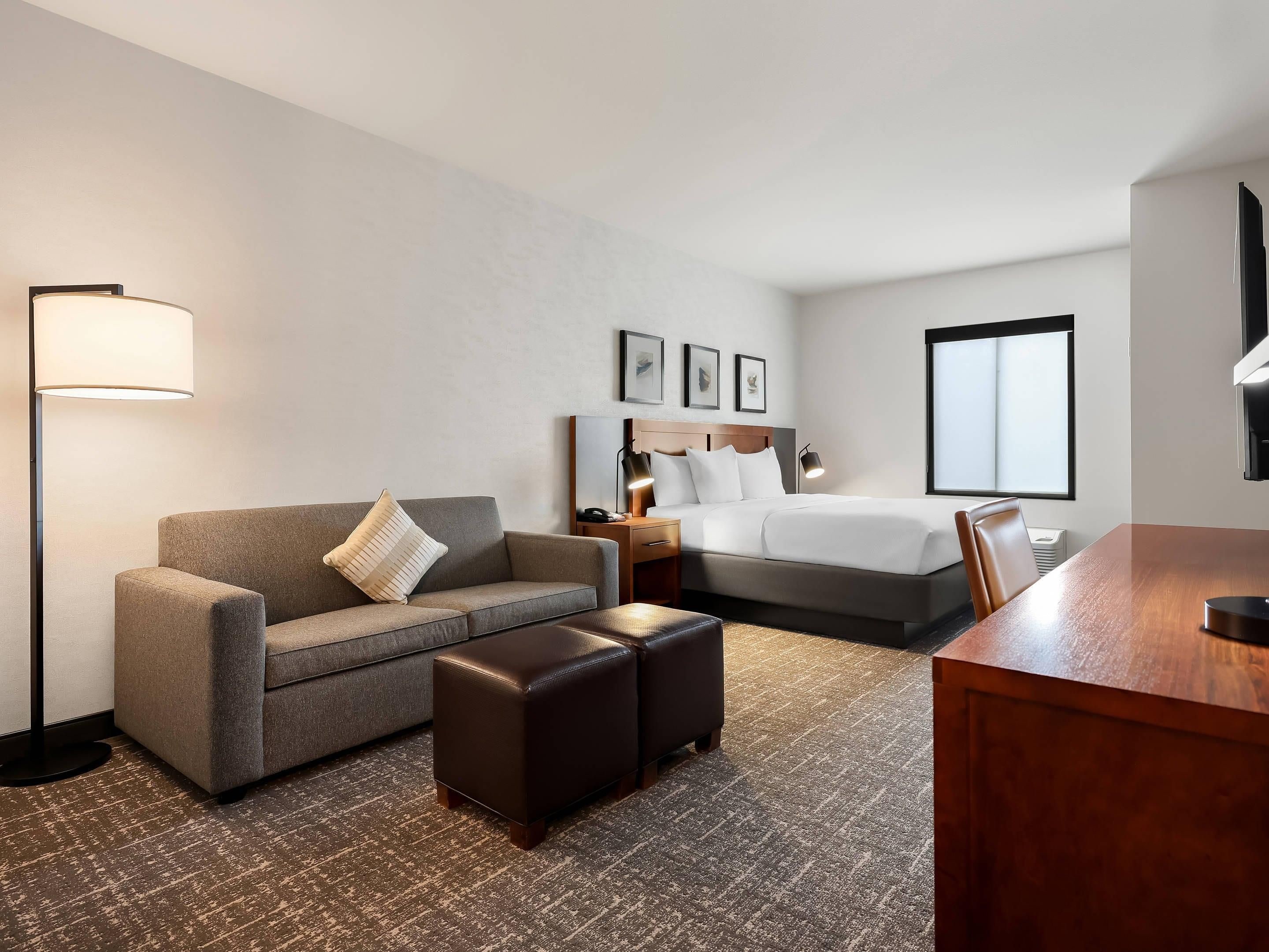 A hotel room with a sofa, a bed, a desk, and a lamp.
