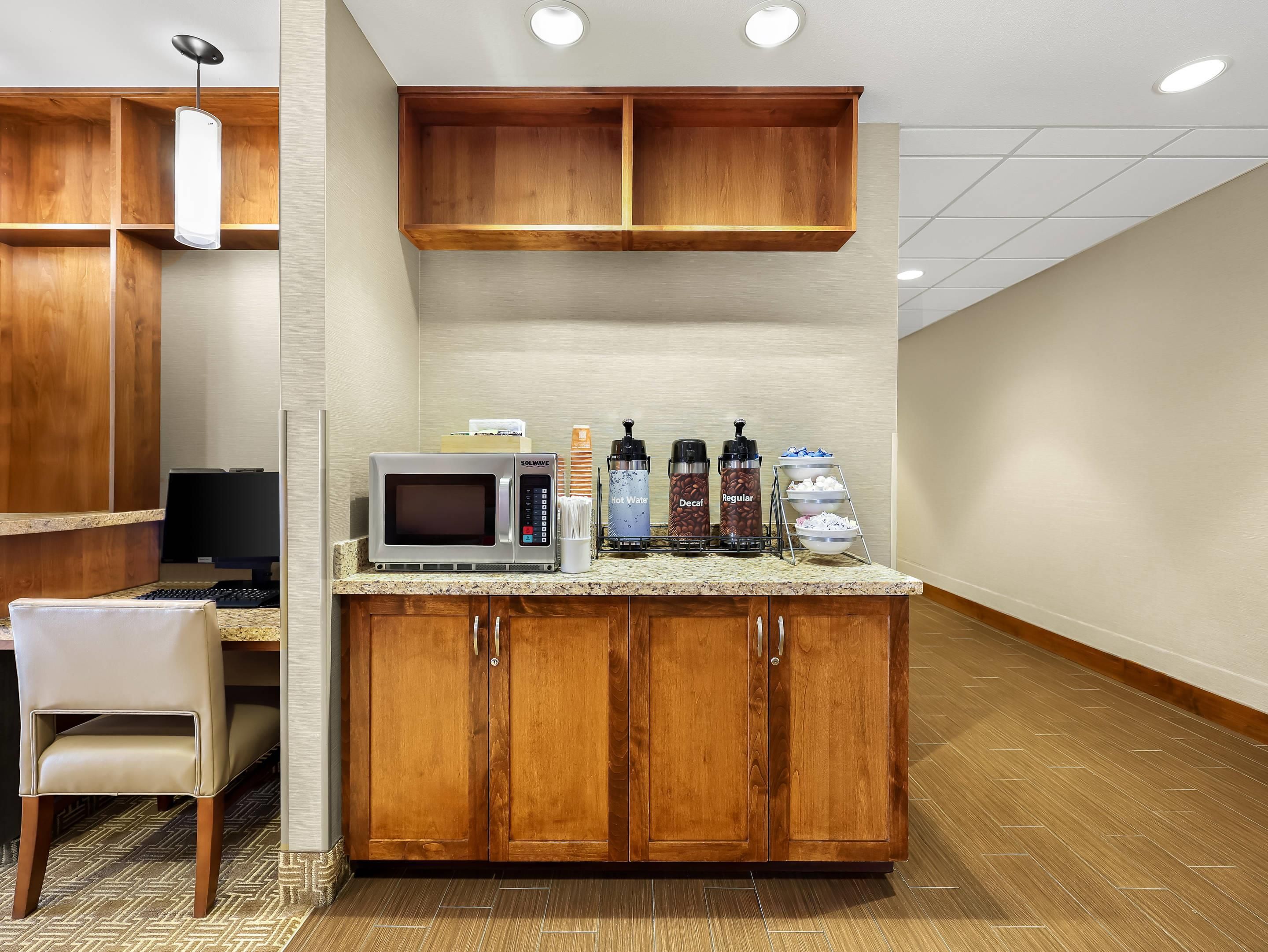 A hotel room with a kitchenette, a microwave, a coffee station, a desk, and a chair.