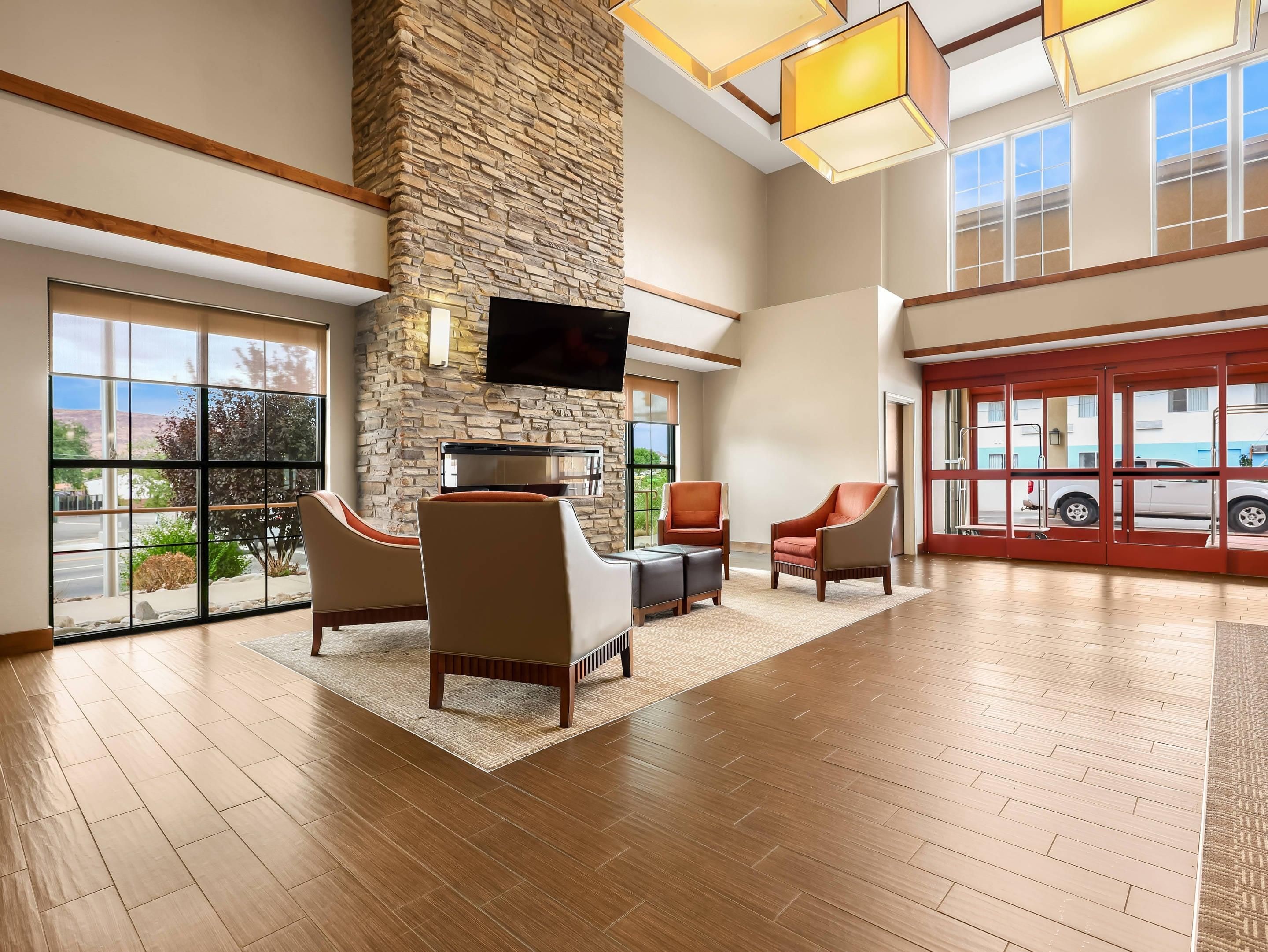 A spacious lobby with a stone wall, comfortable seating, a flat-screen TV, and large windows offering a view of the outside.
