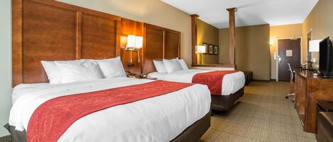A hotel room with two beds, each with white linens and red throw blankets, wooden headboards, and bedside lamps.