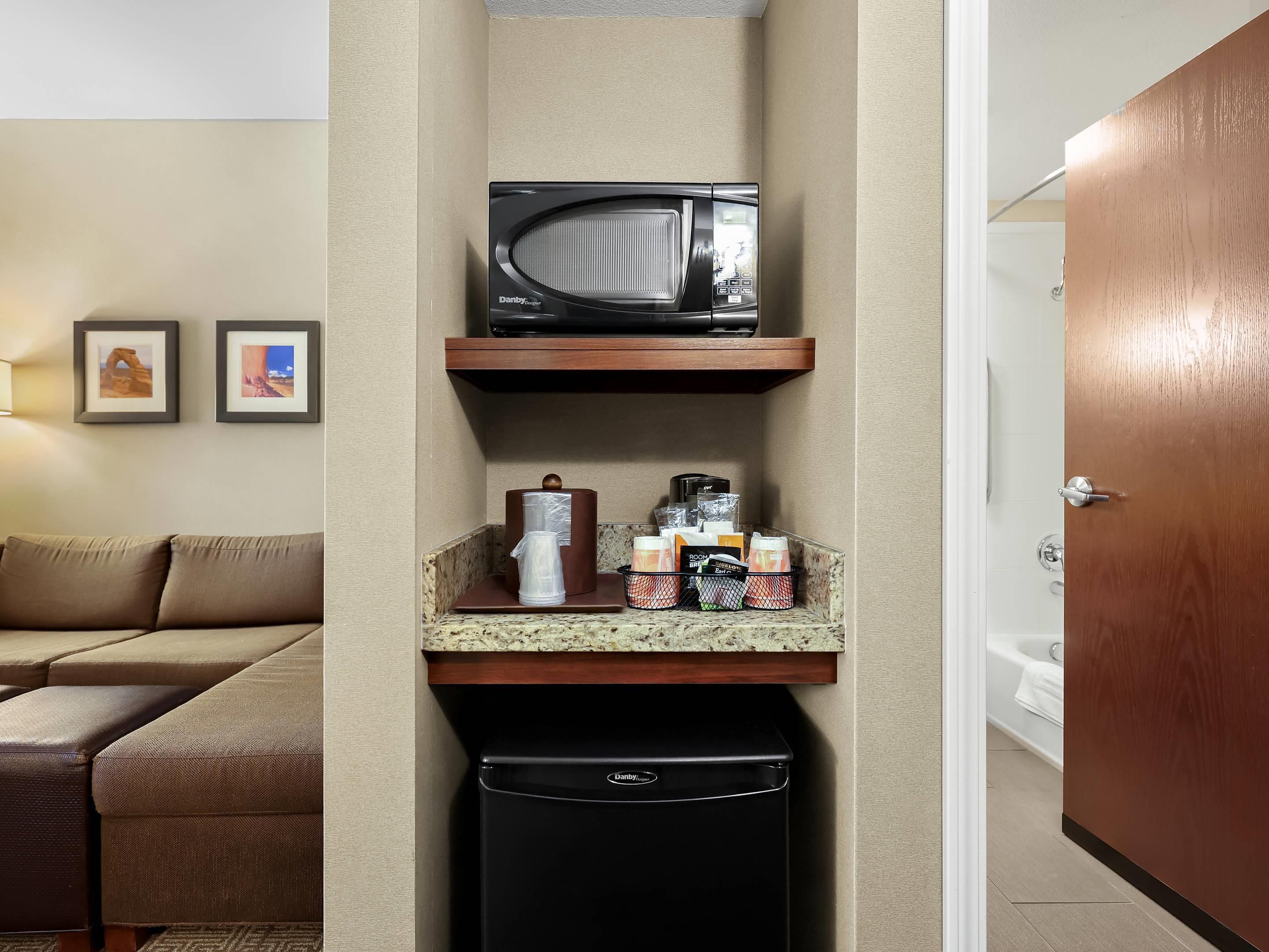 Una kitchenette funcional con microondas, cafetera y contenedores de almacenamiento en la encimera.