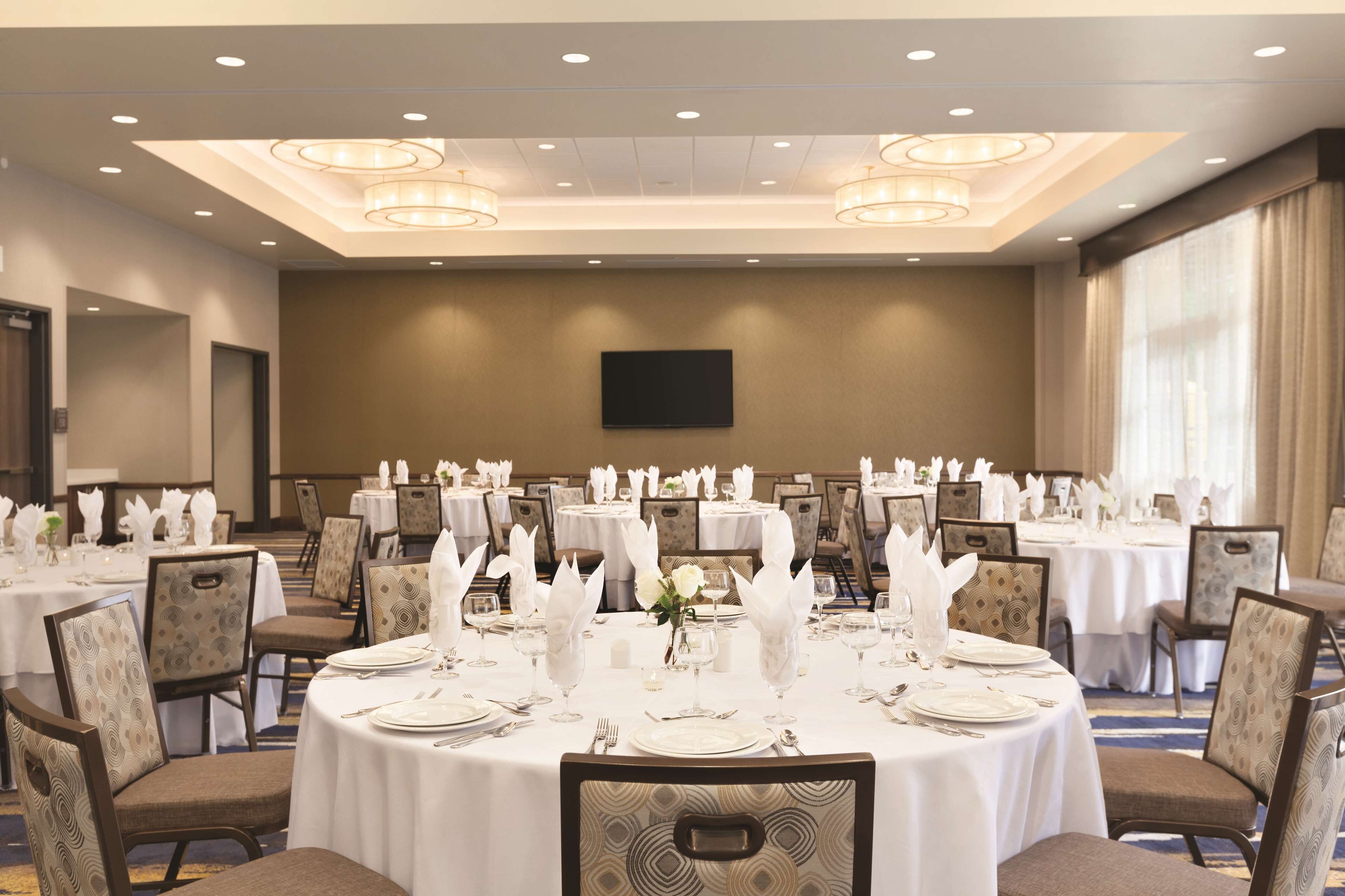 A banquet hall with round tables set for dining, equipped with white tablecloths, chairs, and centerpieces.