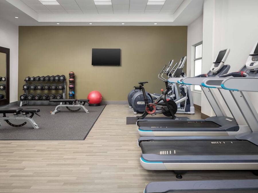 Een sportschool met loopbanden, gewichten, een hometrainer en een rode fitnessbal.