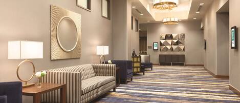A hotel lobby with a striped sofa, a round mirror, a small table with a vase, and a patterned carpet.