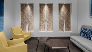Un área de espera moderna con sillas amarillas, un sofá gris y una mesa de centro de madera.