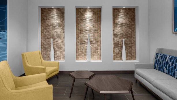 A modern waiting area with yellow chairs, a grey sofa, and a wooden coffee table. - Holiday Inn Express & Suites Midland South I-20 by IHG (Midland)