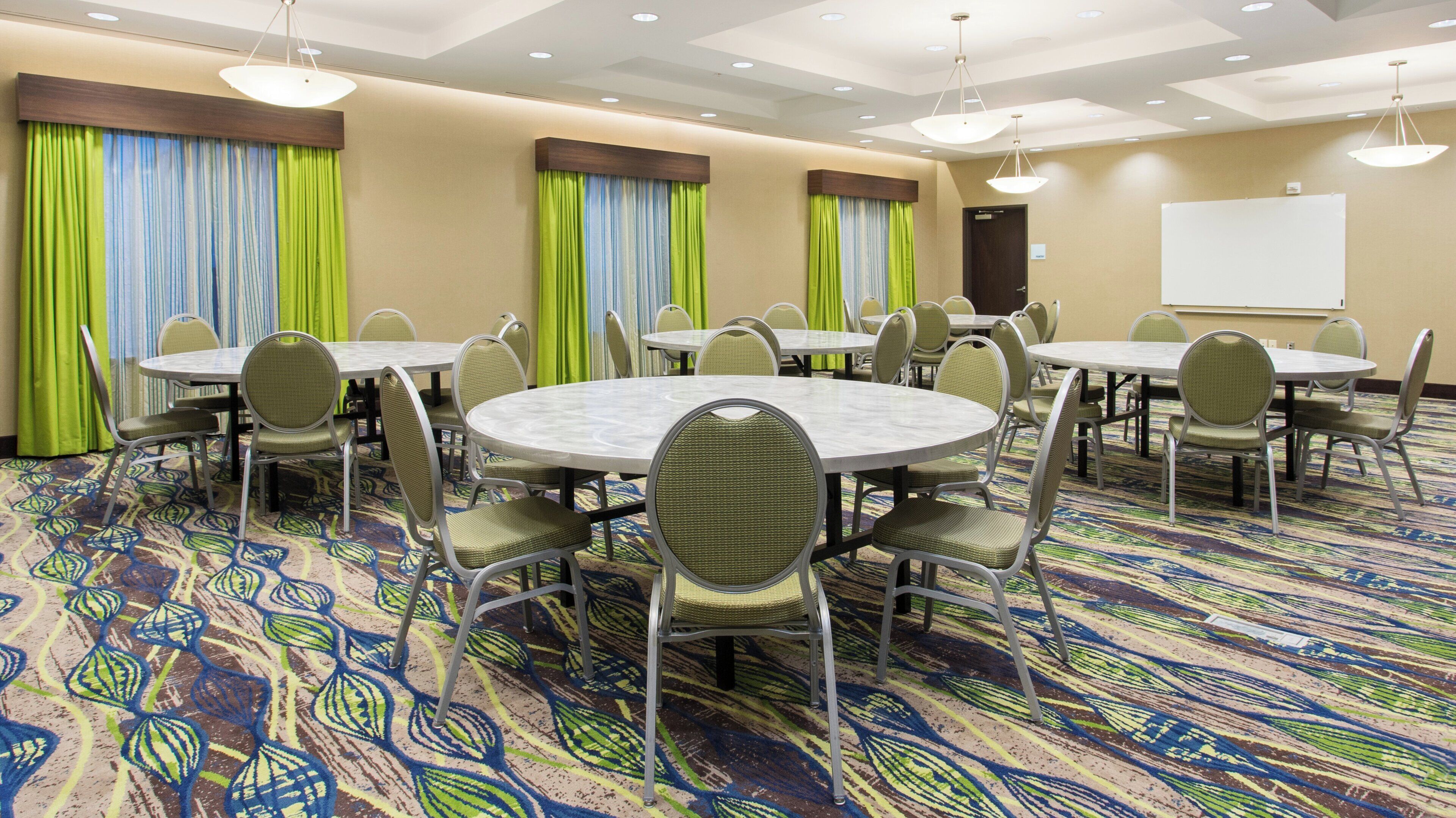 A conference room with round tables and chairs, a patterned carpet, and a whiteboard on the wall.