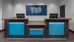 A reception desk with a blue accent panel, two monitors, and a logo on the wall. - Holiday Inn Express & Suites Midland South I-20 by IHG (Midland)