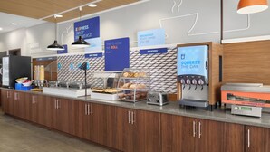 A breakfast area with a counter, food display, and a digital screen. - Holiday Inn Express & Suites Midland South I-20 by IHG (Midland)