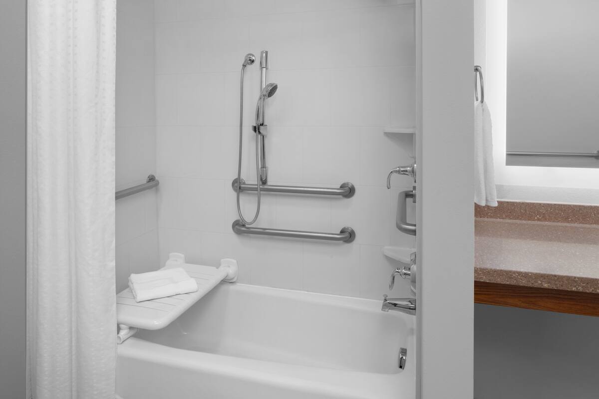 Une salle de bain avec une baignoire blanche, une douche équipée d’un pommeau de douche amovible et d’une barre d’appui.