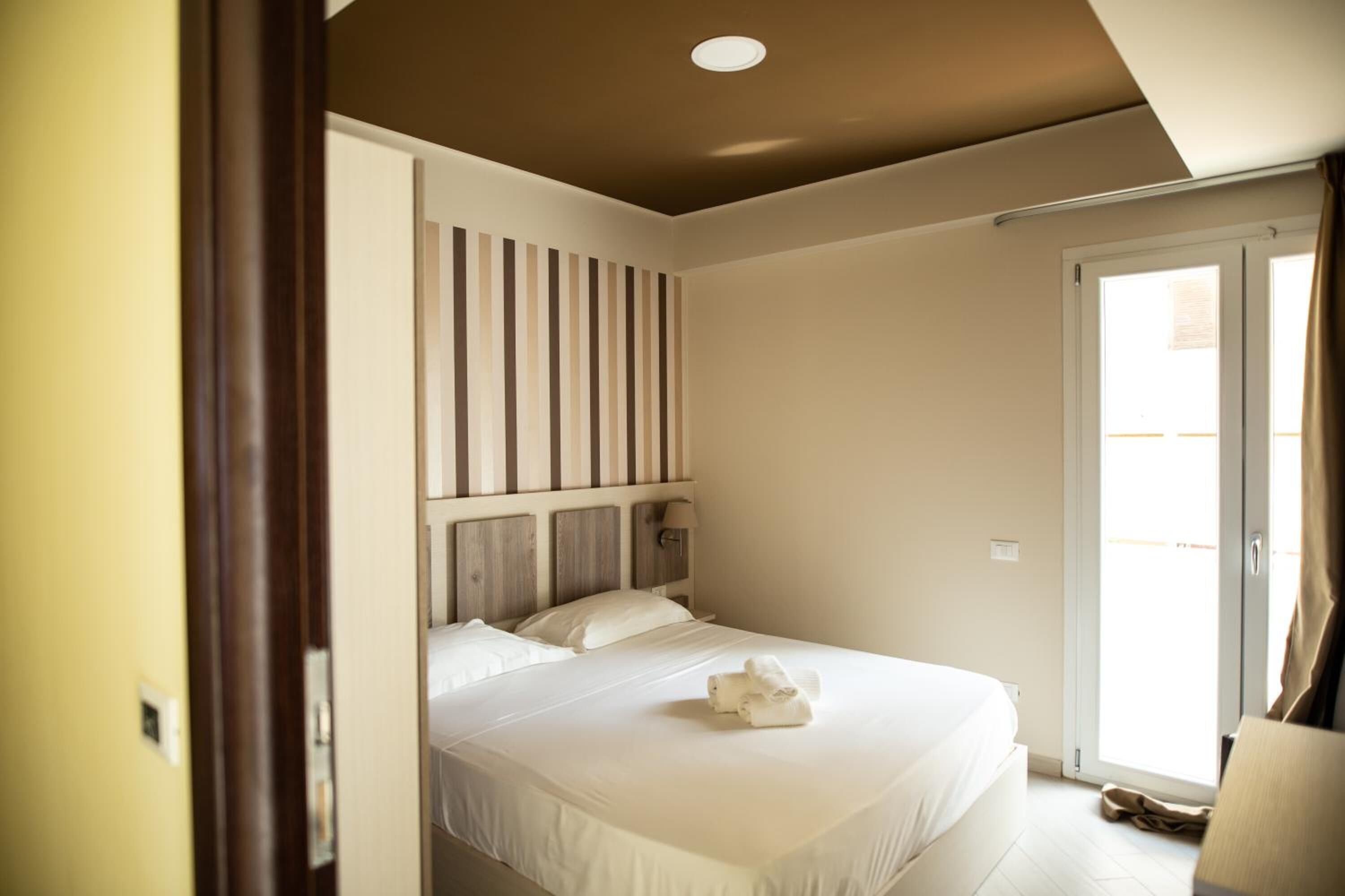 A bedroom with a bed, a headboard with vertical wooden slats, a nightstand, and a window with curtains.