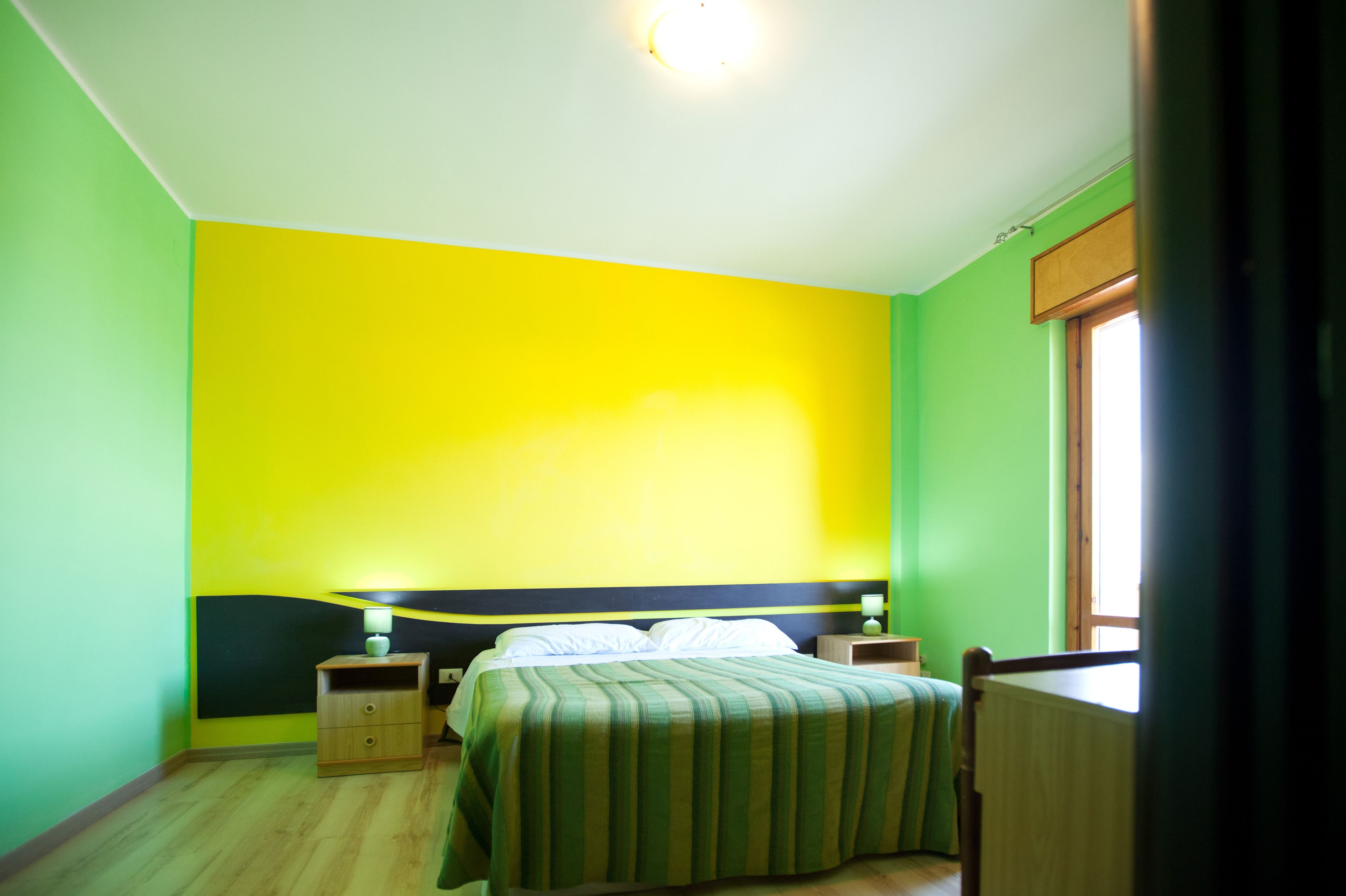 Una habitació amb un llit, una tauleta de nit, una làmpada i una finestra.