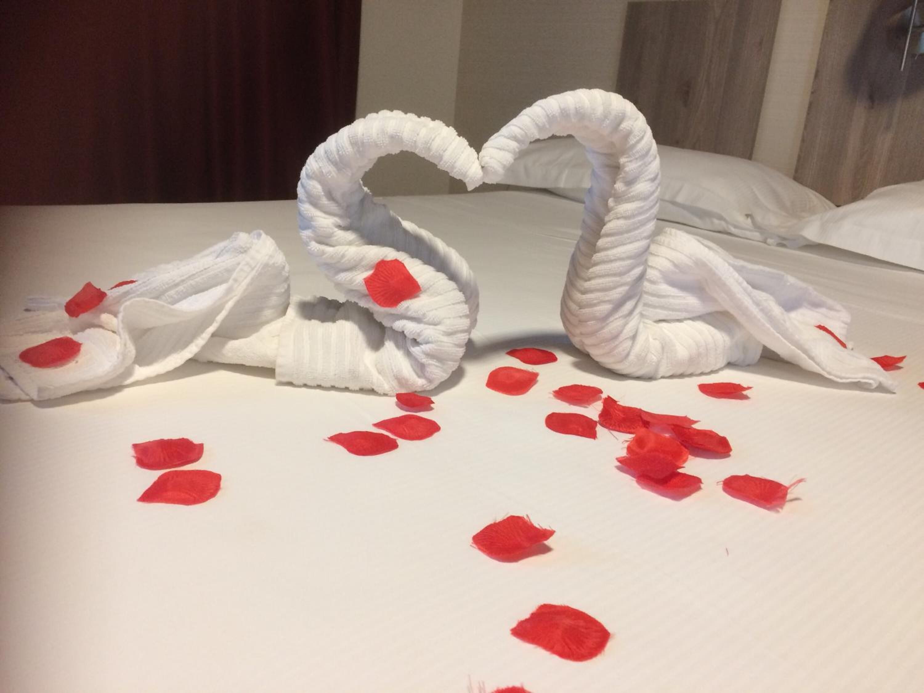 Una cama con sábanas blancas y pétalos de rosa roja esparcidos.