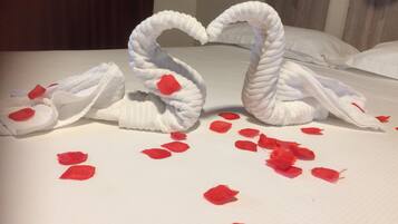 Un letto con lenzuola bianche e petali di rosa rossa sparsi sopra.