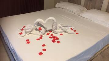 A bed with white linens and a decorative swan made of towels on the bedspread, with red rose petals scattered around.
