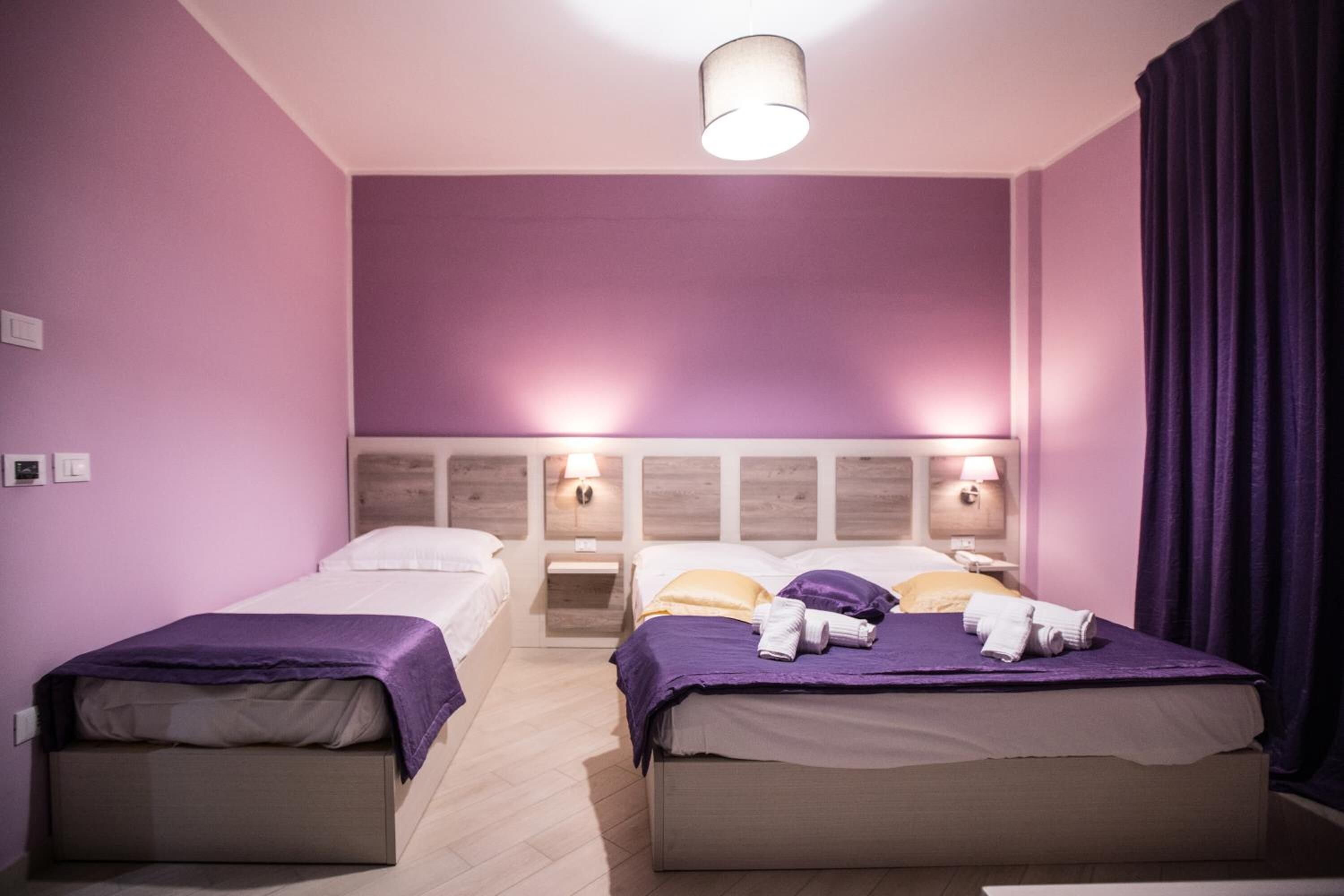 A hotel room with two beds, each with a headboard, and a nightstand with a lamp between them.