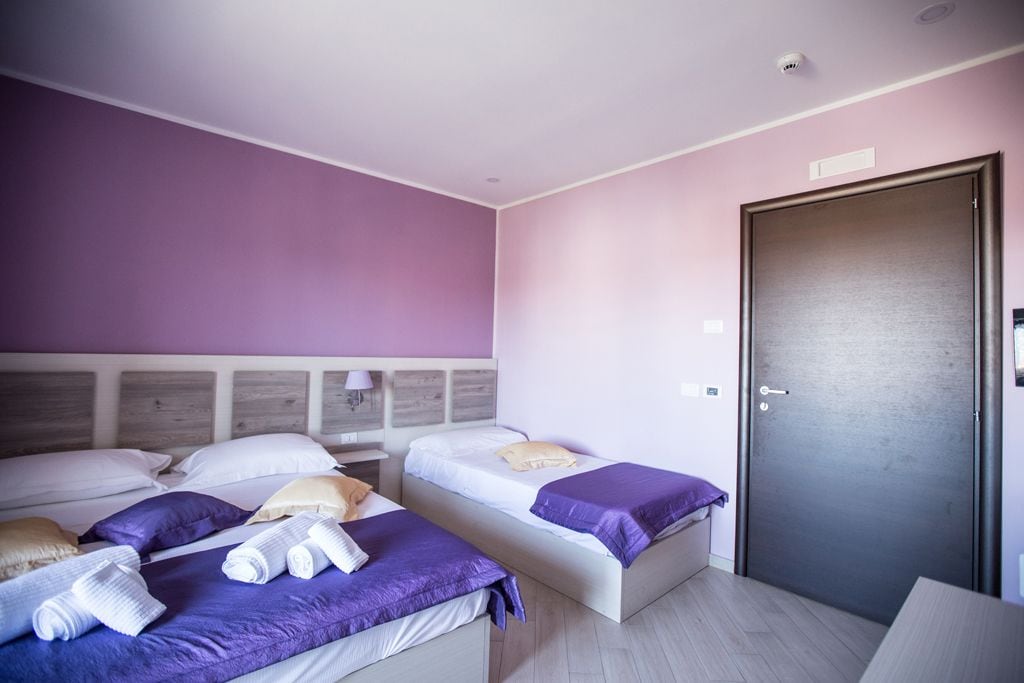 Habitación de hotel con dos camas, una puerta y una mesita de noche con lámpara.