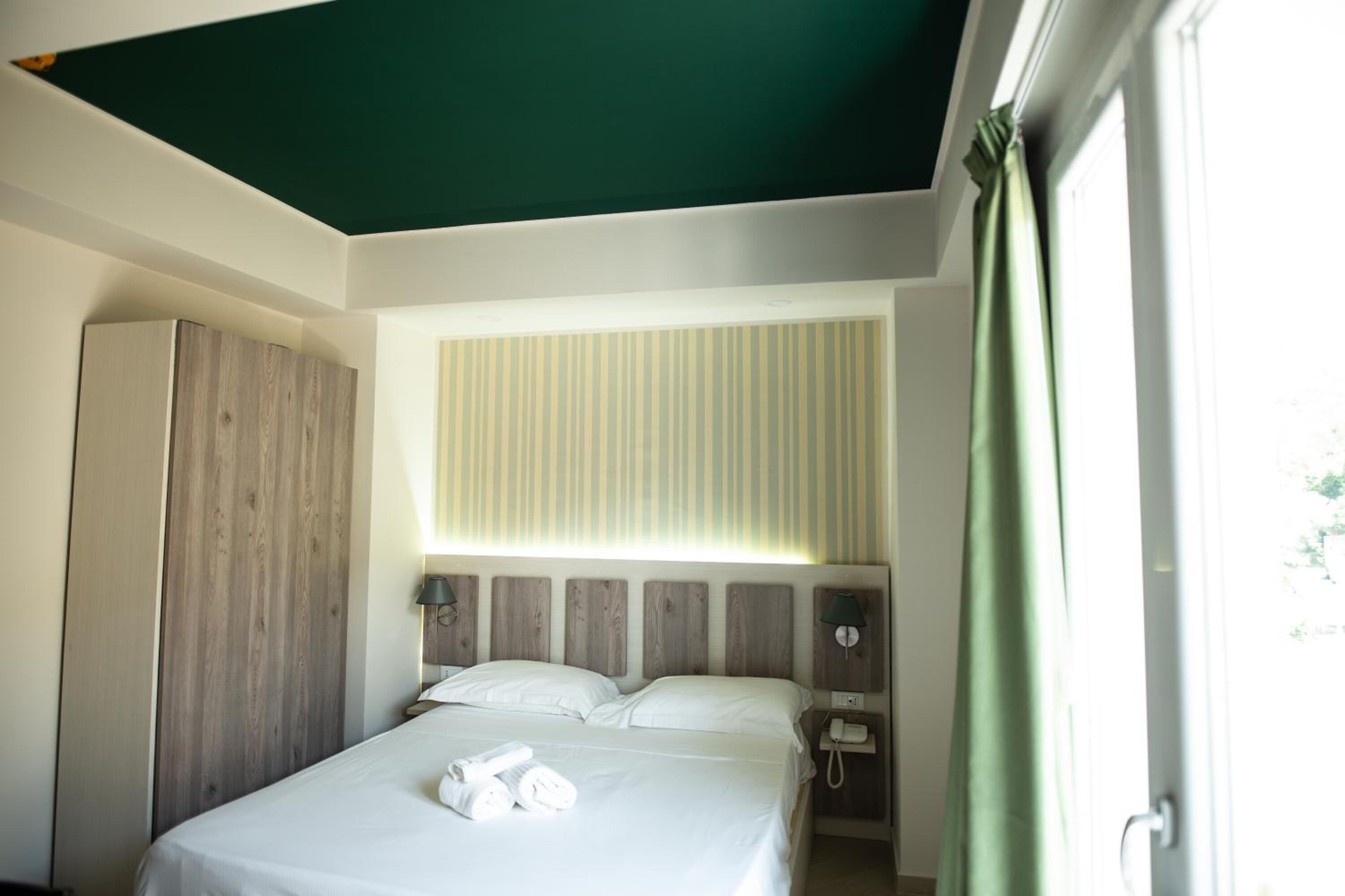 A bedroom with a bed, a nightstand, a telephone, and a window with curtains.
