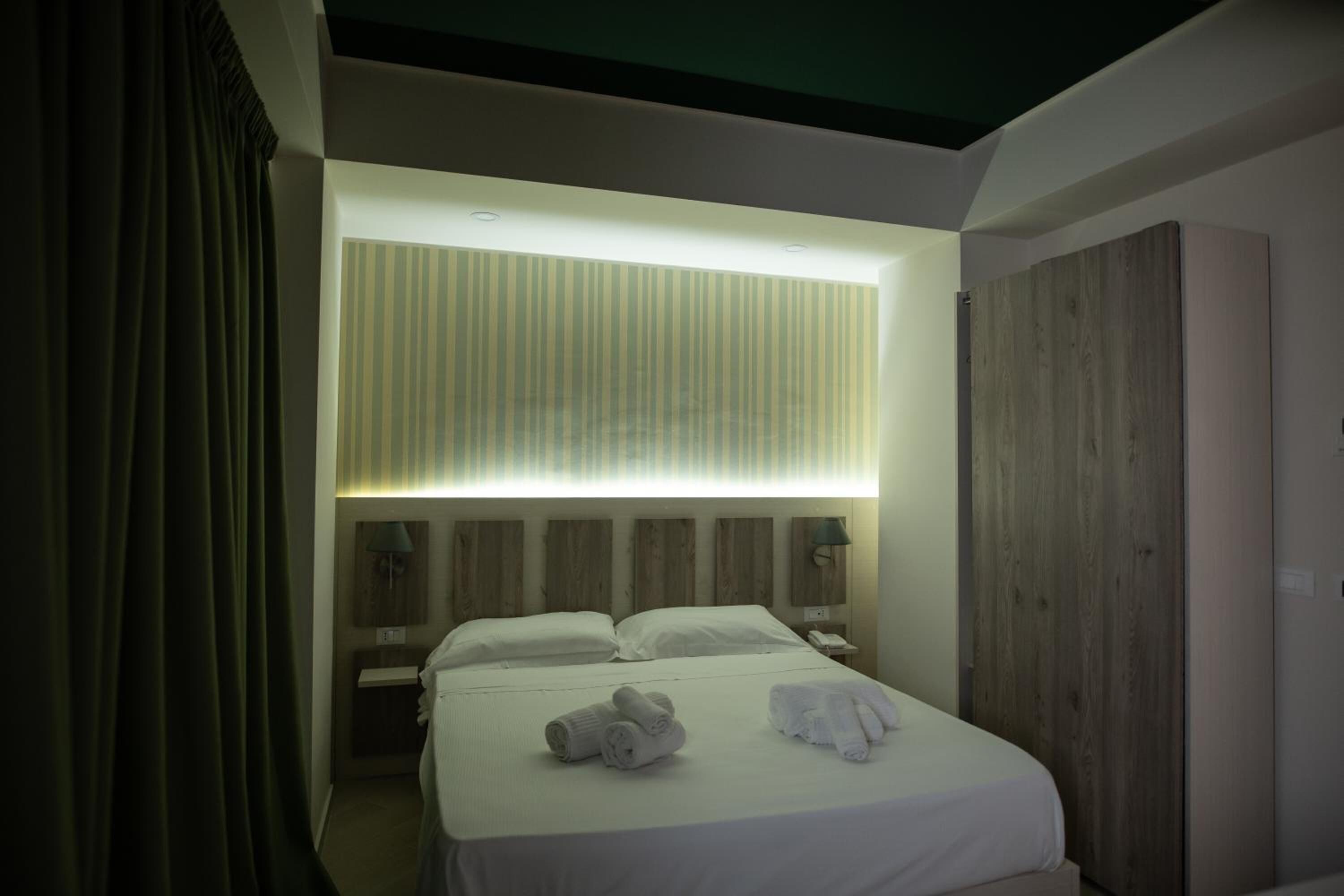 Una habitación de hotel moderna con una cama grande, un armario de madera y una mesita de noche con lámpara.