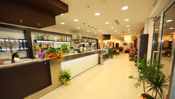 A hotel lobby with a reception desk, a coffee machine, and various plants. - Hotel Cliché (San Lucido)