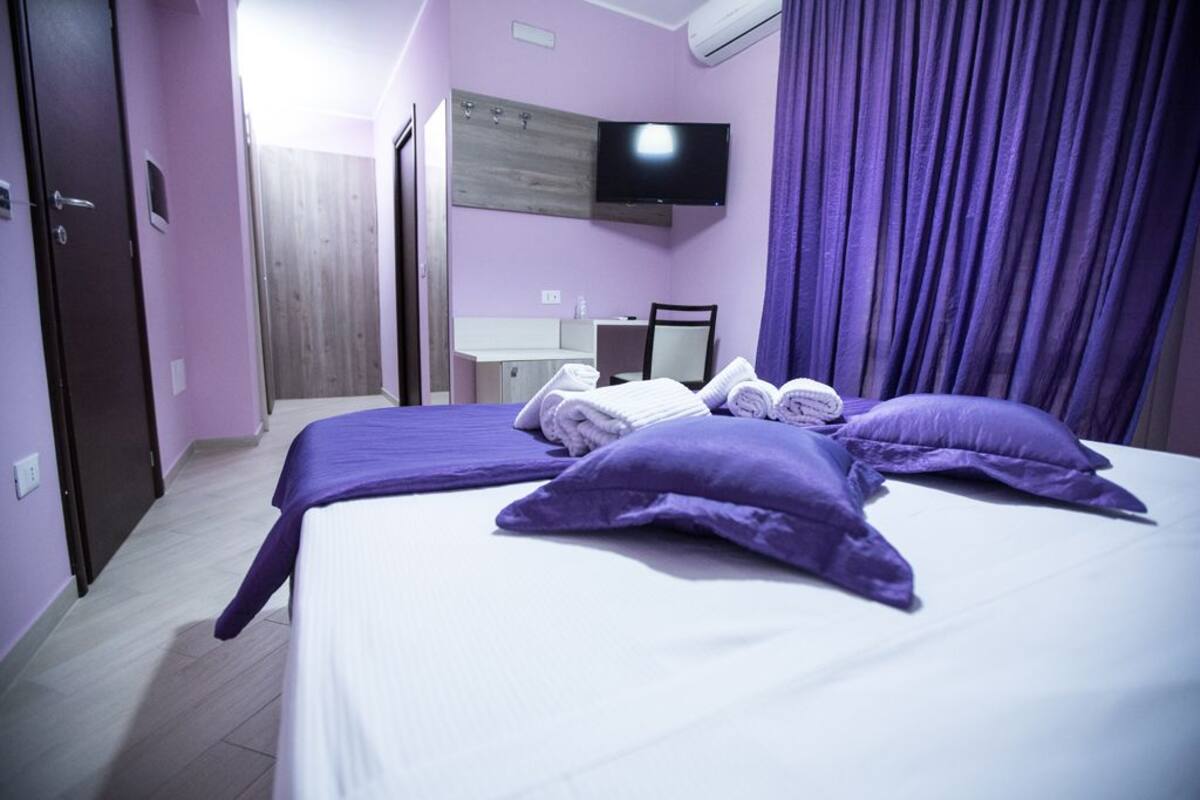 A hotel room with a large bed, a desk, a mirror, and a TV on the wall.