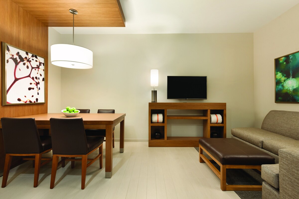 A modern living room with a wooden dining table, chairs, a TV stand, and a sofa.
