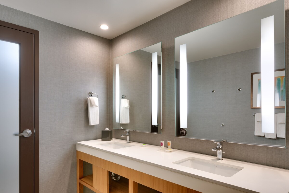 A modern bathroom with two sinks, a large mirror, and a wooden vanity.