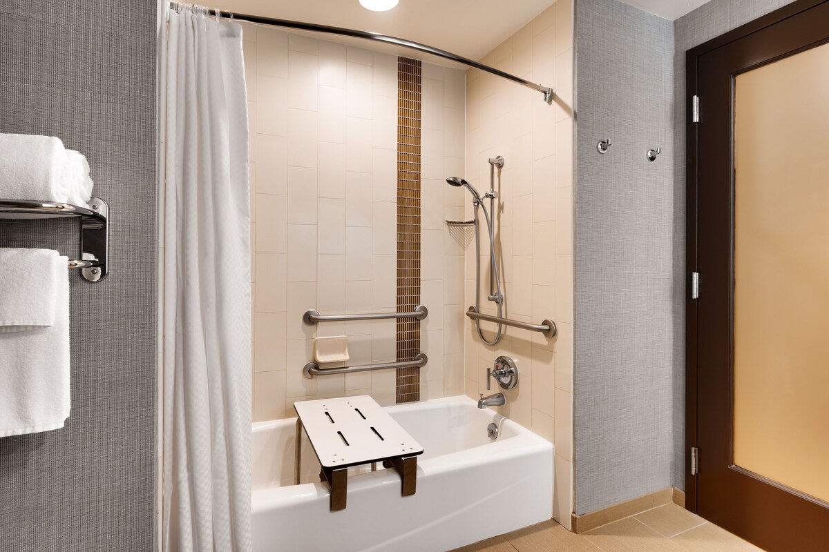 A modern bathroom with a walk-in shower, grab bars, a towel rack, and a bathtub.
