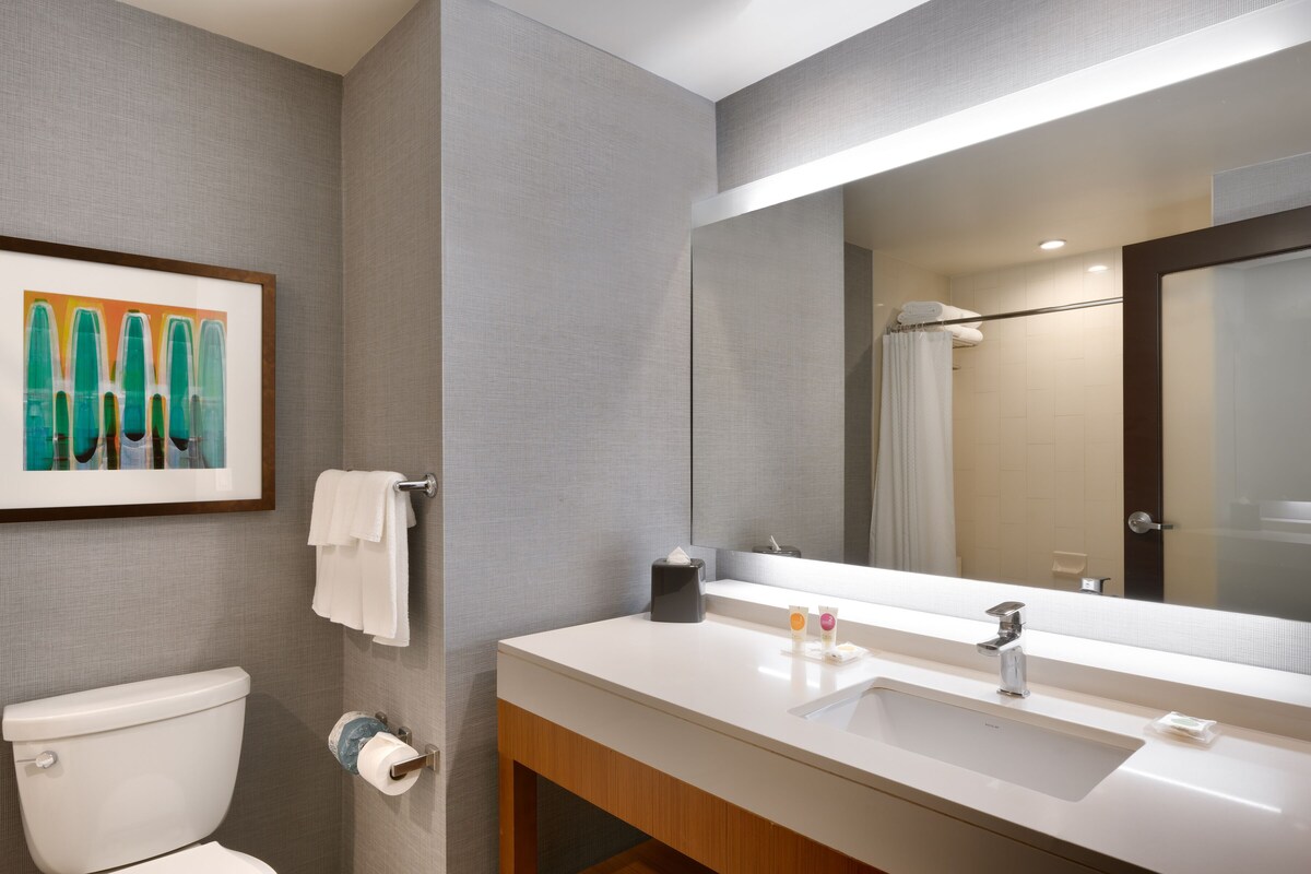 A modern bathroom with a toilet, sink, and mirror. There is a framed artwork on the wall and a towel rack.