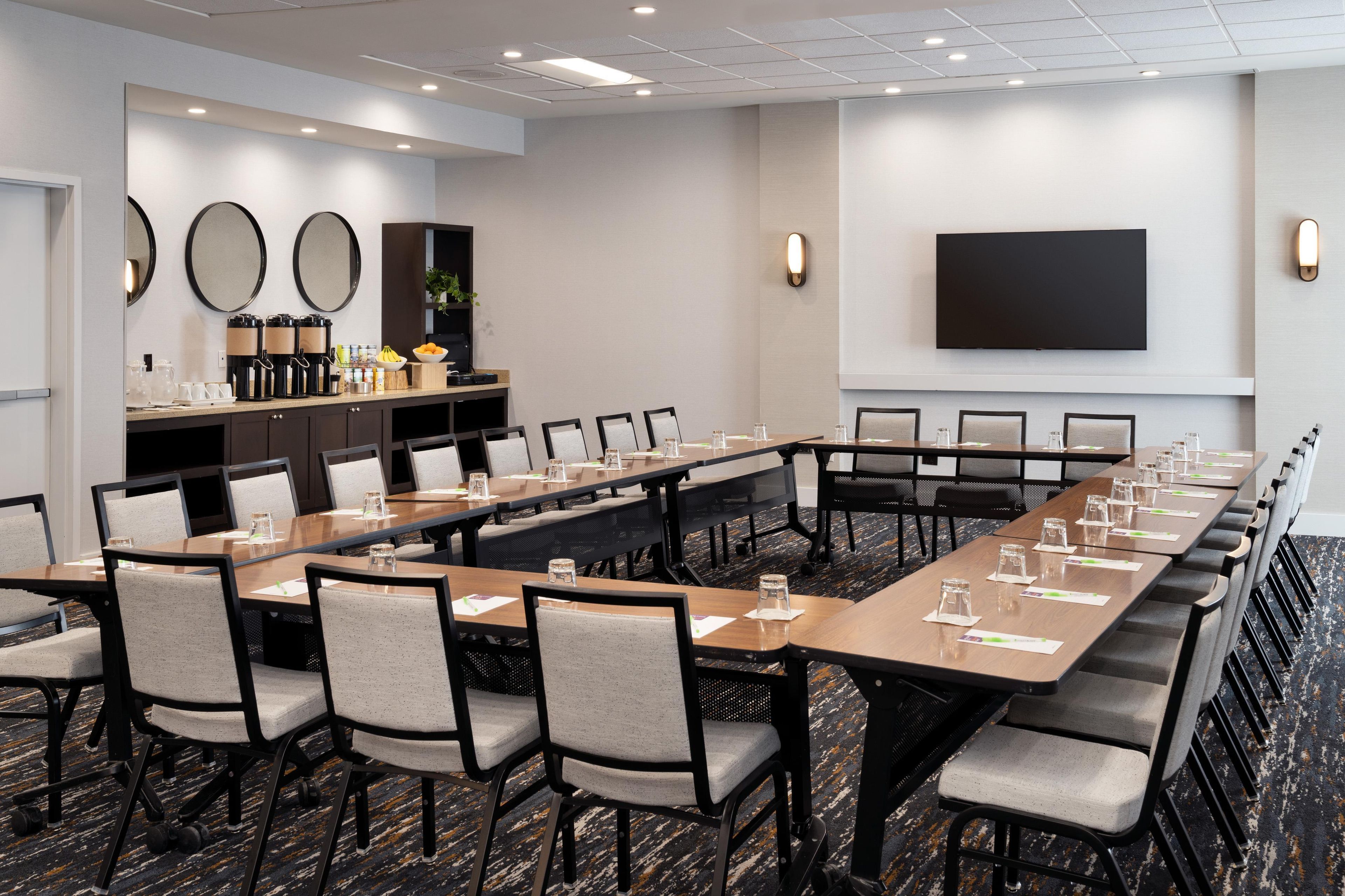 A conference room with a long table, chairs, a coffee station, and a flat-screen TV on the wall.