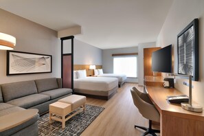 Une chambre d’hôtel équipée d’un canapé, d’un lit, d’un bureau avec une chaise, d’une télévision et d’œuvres d’art accrochées aux murs.